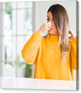 Young Beautiful Woman Wearing Winter Sweater At Home Smelling Something Stinky And Disgusting, Intolerable Smell, Holding Breath With Fingers On Nose. Bad Smells Concept. Canvas Print