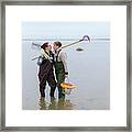 Same Sex Female Couple In Waders Standing In Ocean Holding Clam Rakes Framed Print