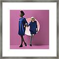 Two Women Peeking Out Of Round Opening In Coloured Wall #1 Framed Print
