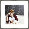 An Intelligent Looking Student Working At A Desk In A Classroom, With A Blackboard Behind Him Covered In Algebra Equations Framed Print