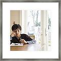 Boy Sitting At Table, Holding Pen To Paper Framed Print