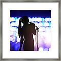 Silhouette of woman with microphone singing on concert stage in front of crowd Framed Print