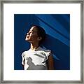 Thoughtful Woman Standing Against Blue Wall Framed Print