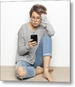 Portrait Of Young Woman With Wireless Earphones Sitting On The Floor Looking At Cell Phone Metal Print