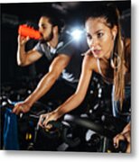 Two Young People Exercising On Exercise Bike At Gym Metal Print