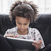 Girl Sitting On Sofa Using Digital Tablet And Headphones Art Print
