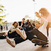 Laughing Friends Photographing Man Falling From Skateboard While Woman Pushing Him At Park Art Print