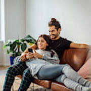 Young Couple With Mobile Phone Relaxing On Sofa Art Print