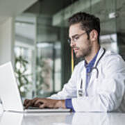 Male Doctor Using Laptop At Desk In Clinic Art Print