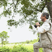 Senior Man Standing By Tree Holding Binoculars, Side View Art Print