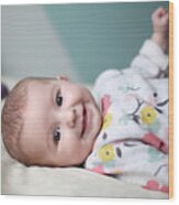 A Baby Girl Smiling On A Bed Wood Print