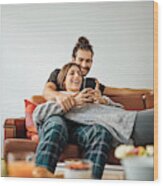Young Couple With Smart Phone Relaxing On Sofa Wood Print