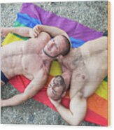 Lgbt Pride Concept. Couple Of Muscular Gay Bears Lying On The Sand On The Beach Over The Rainbow Flag Looking At The Infinite Sky. Wood Print