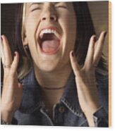 A Caucasian Young Woman With Brown And Blond Streaked Hair Wearing A Jean Jacket Is Screaming With Eyes Closed And Hands Raised Near Her Face Wood Print