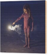 Little girl playing with bengal fire on the beach at dusk. Wood Print