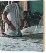 Rear View Of Senior Asian Man Suffering From Backache, Massaging Aching Muscles While Sitting On Bed. Elderly And Health Issues Concept Wood Print